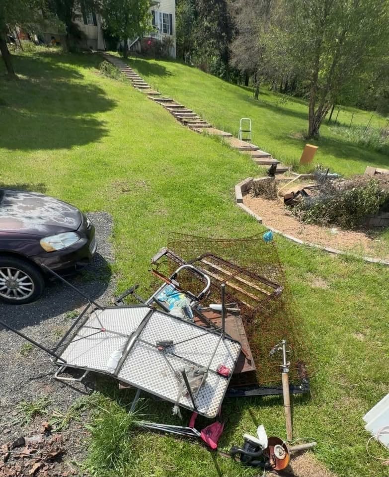 Residential hillside with metal cart, trailer, and parked car on lawn, wooden steps leading uphill toward house