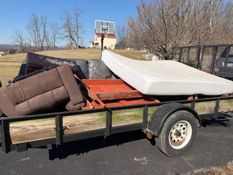 Utility trailer loaded with rolled fabric materials and cushioned items in a rural setting